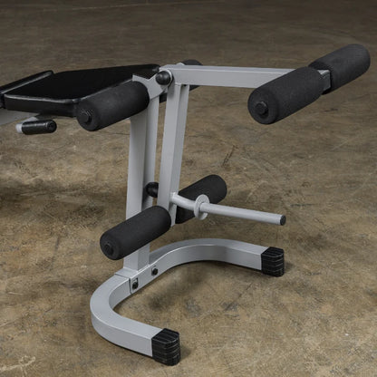 Close-up of a gym equipment piece featuring a padded seat and foam rollers, designed for abdominal workouts, resting on a concrete floor.