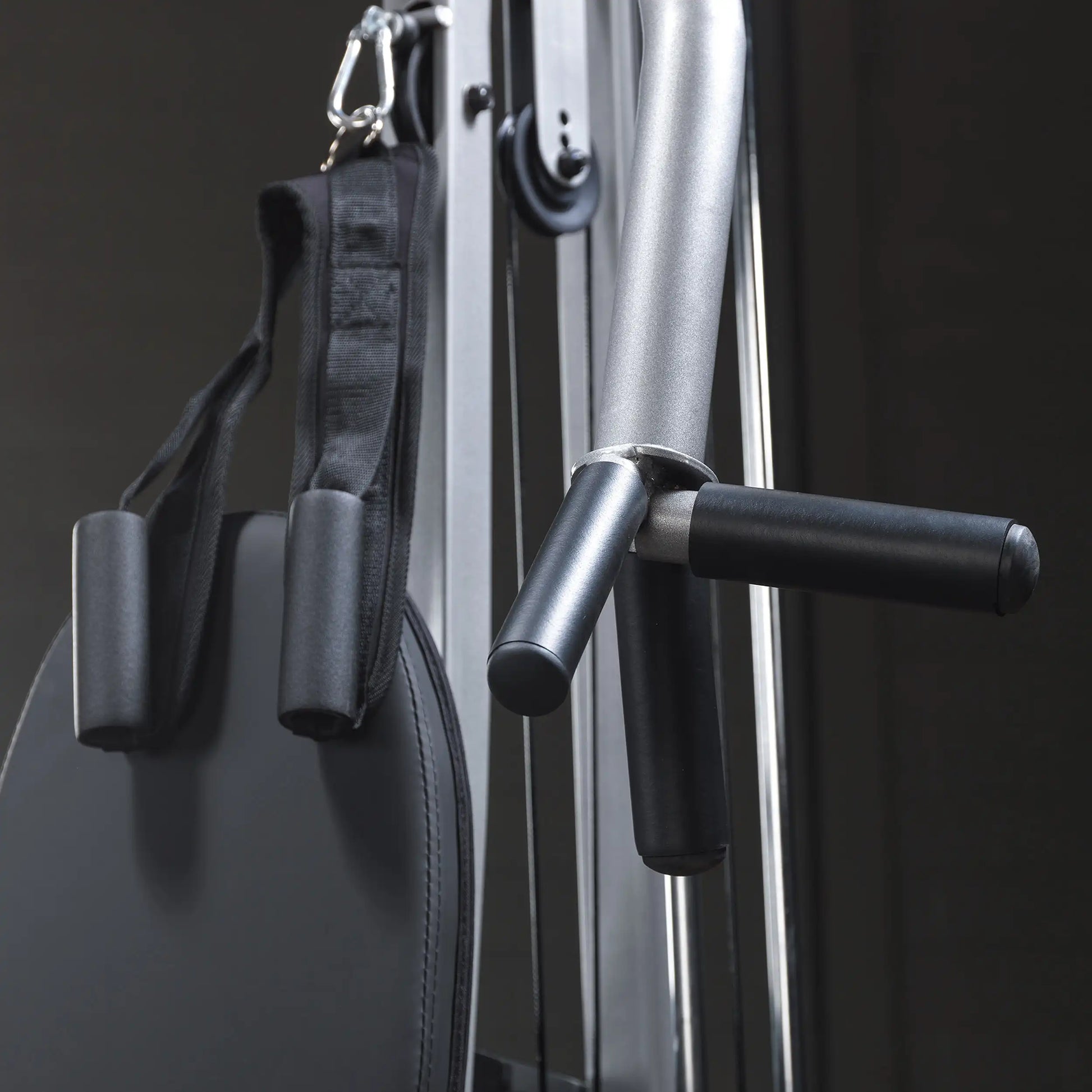Close-up of a fitness machine showing a padded seat, black straps, and handles, with a sleek metallic frame in a dark setting.