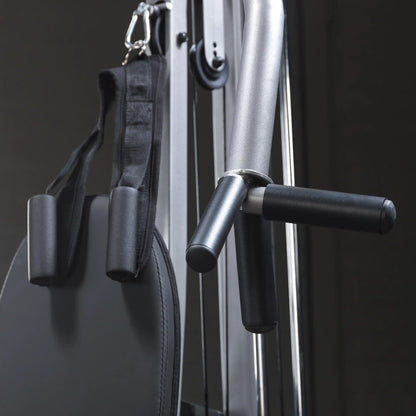 Close-up of a fitness machine showing a padded seat, black straps, and handles, with a sleek metallic frame in a dark setting.