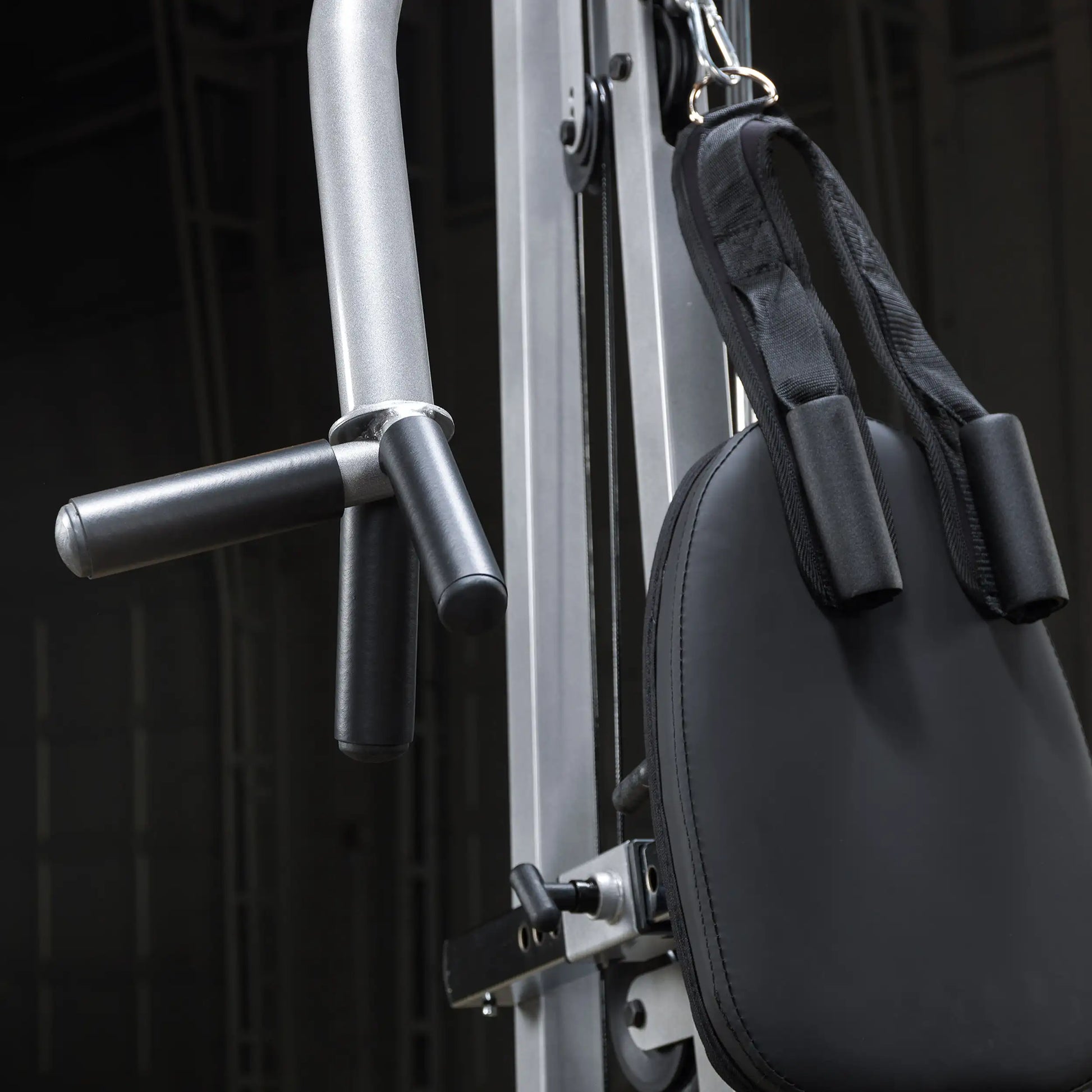 Close-up of a gym cable machine with a black padded handle and a silver frame, showcasing the adjustable components and grips.