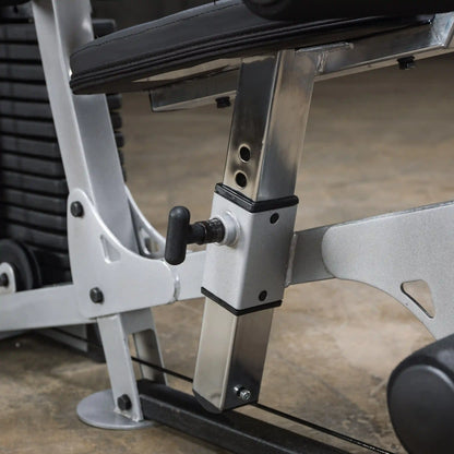 Close-up of a silver and black adjustable weight bench mechanism, showing the adjustment lever and metal supports against a textured floor.