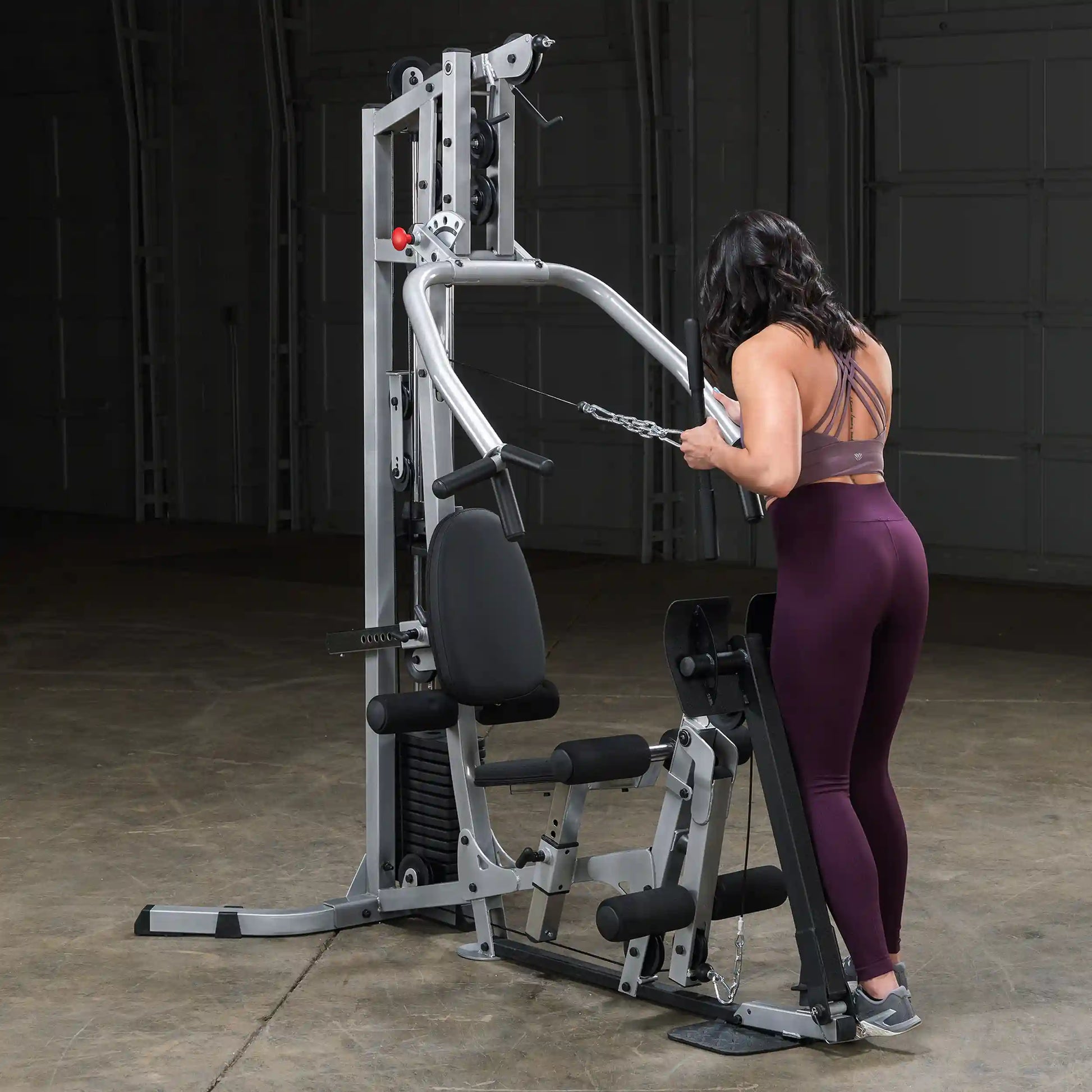A woman in workout attire using a cable machine in a gym setting, focusing on her form while performing an exercise. The machine features adjustable weights and a seated position.
