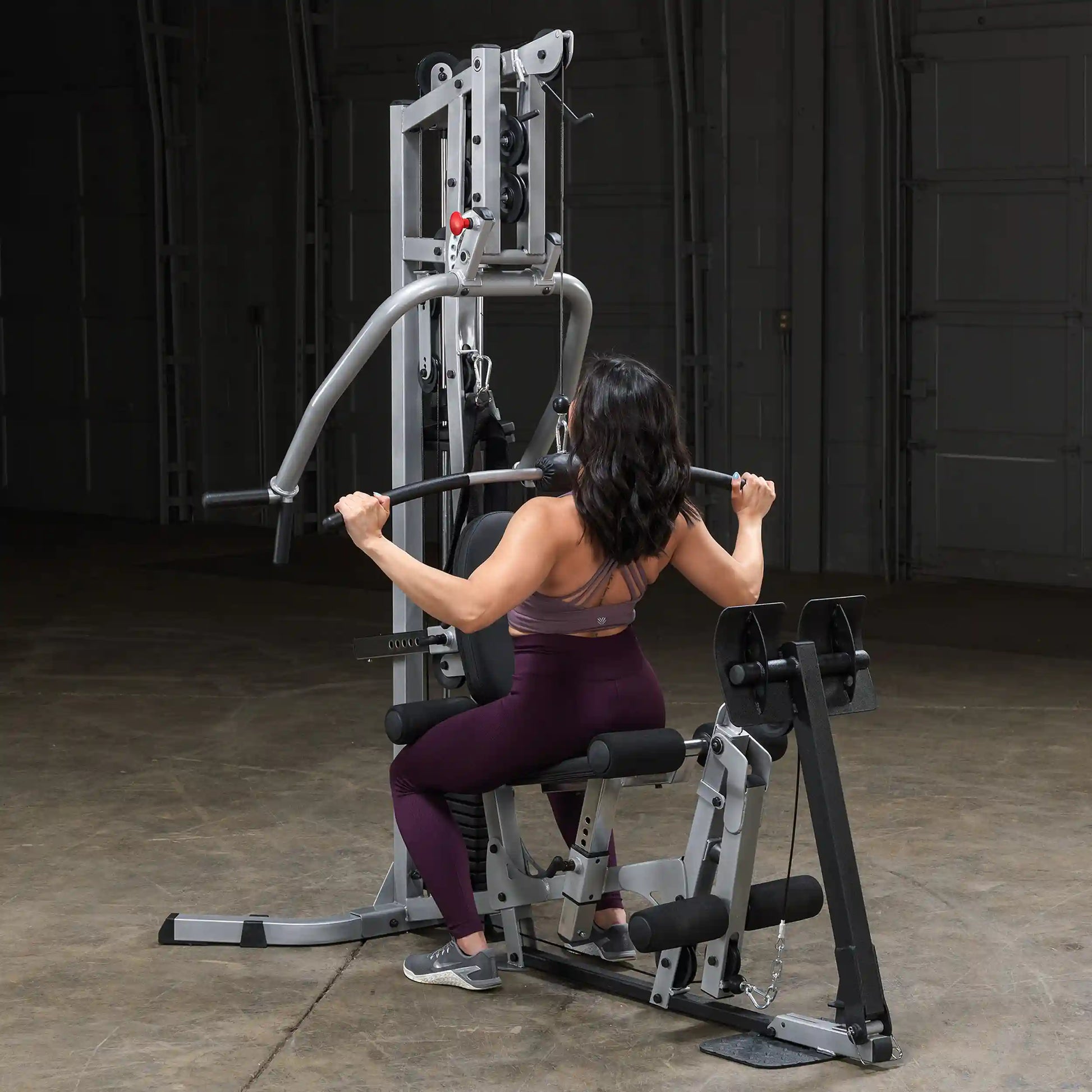 A person performing a seated exercise on a multi-gym machine, gripping the bar with both hands, showcasing a focused workout in a spacious indoor gym environment.