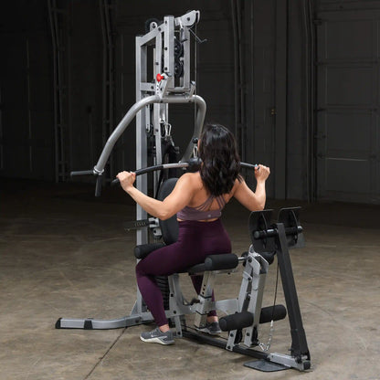 A person performing a seated exercise on a multi-gym machine, gripping the bar with both hands, showcasing a focused workout in a spacious indoor gym environment.