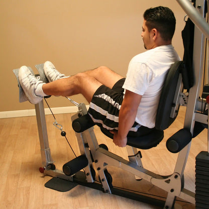 A man performing leg exercises on a leg extension machine in a gym, wearing a white t-shirt and black shorts.