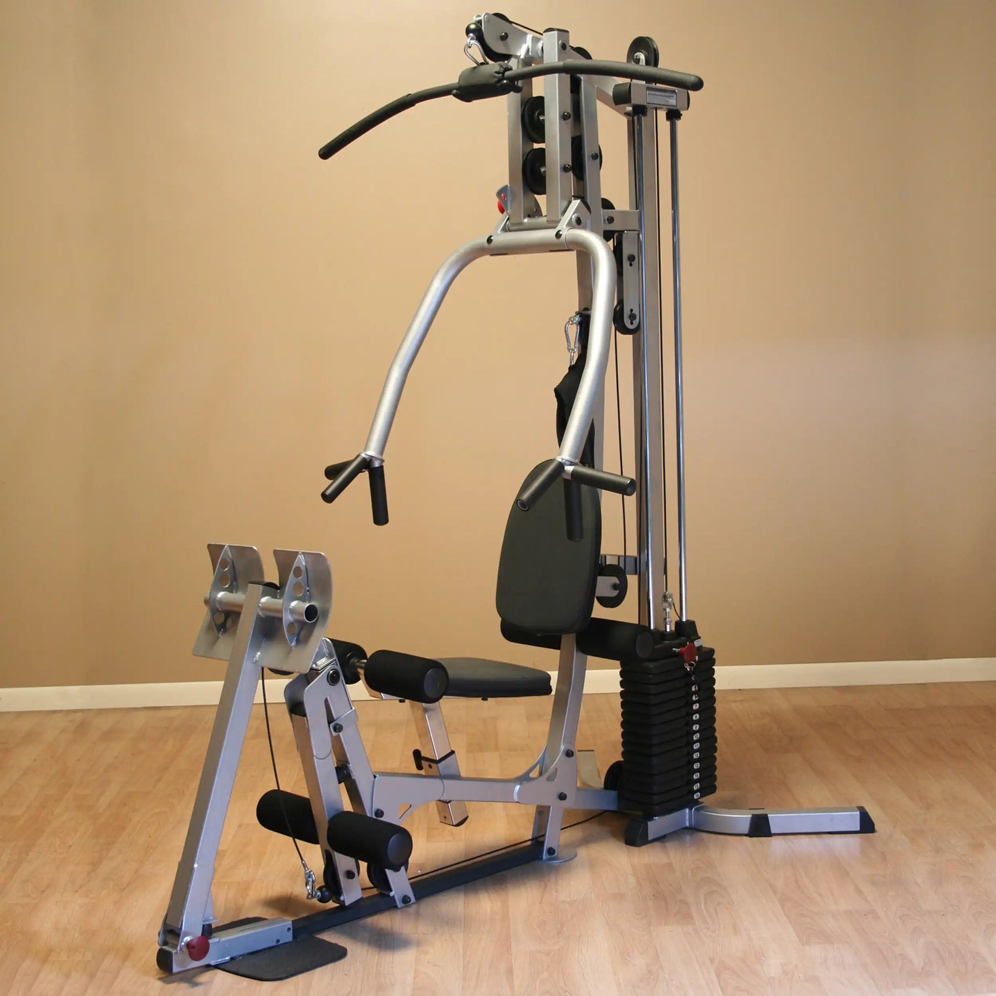 A multi-station home gym equipment with a weight stack, adjustable seat, and various handles for strength training exercises, set against a neutral wall.
