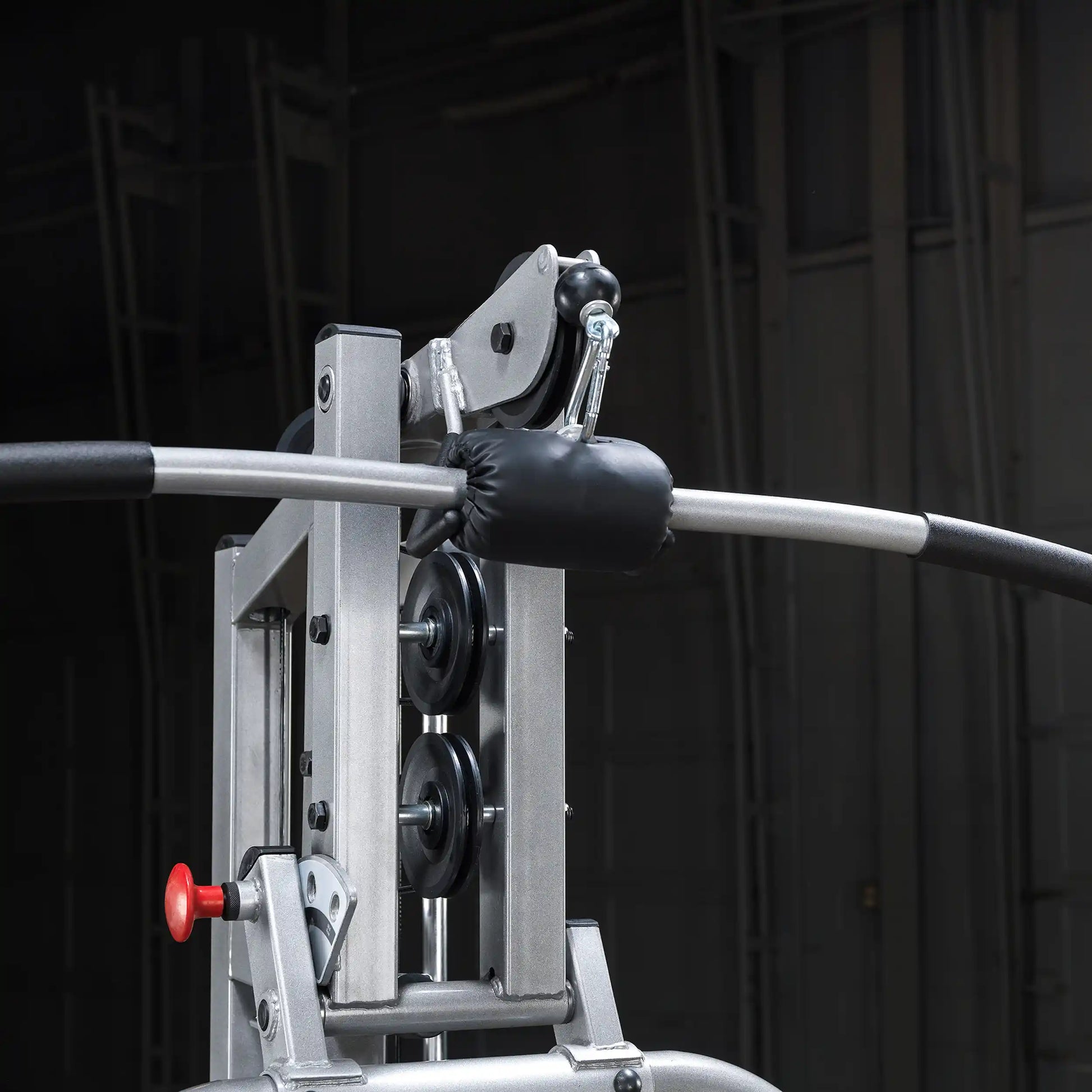 Close-up of a gym cable machine showing the pulley system, a padded handle, and a red adjustment knob, set against a dark background.