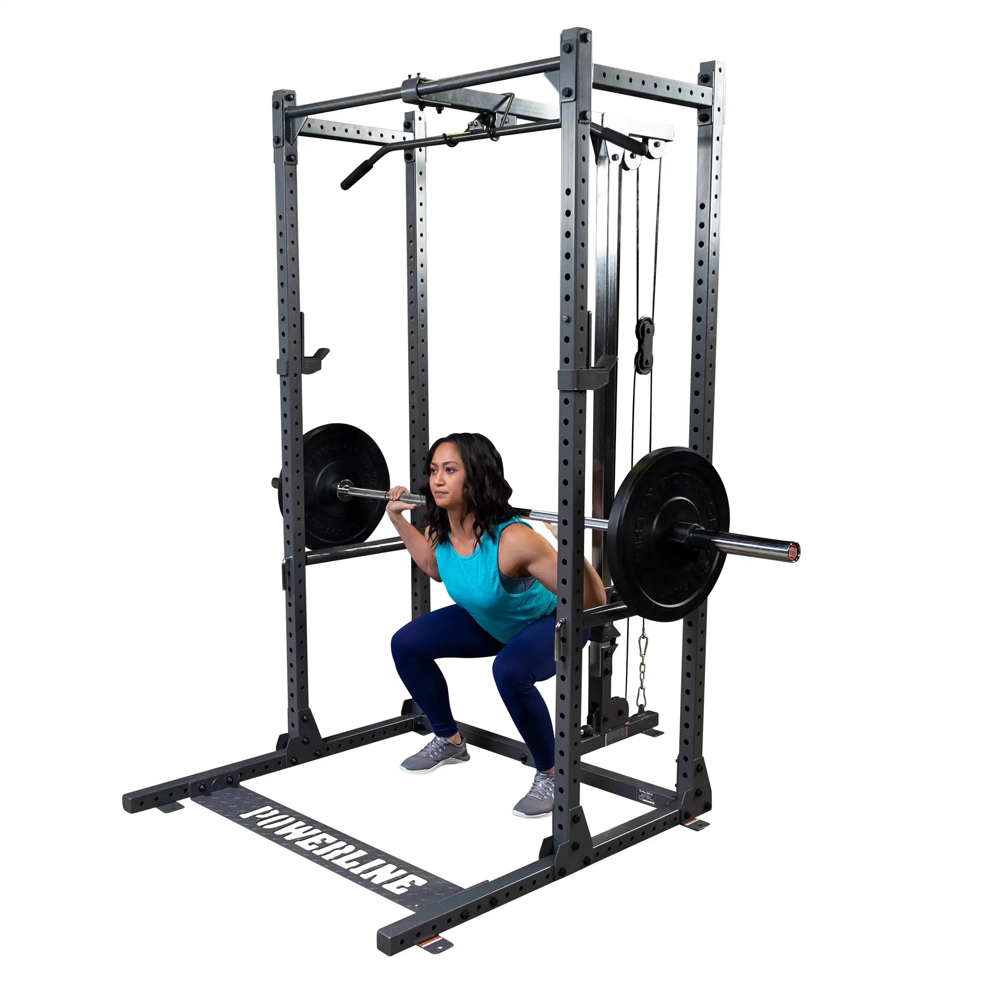 A woman performing a squat with a barbell on her shoulders inside a squat rack, wearing a blue tank top and leggings, with weight plates on the barbell.