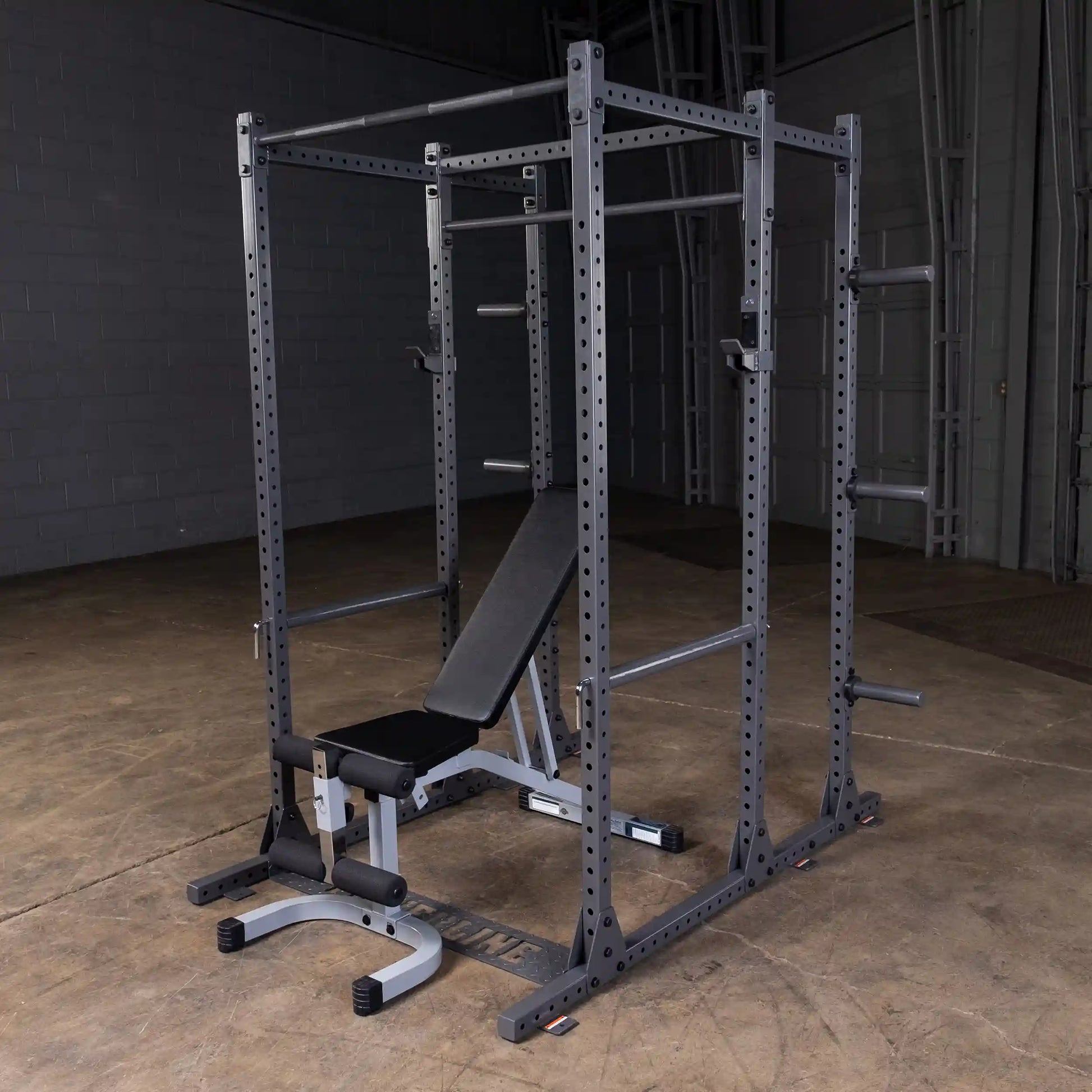 A sturdy black power rack with a bench, designed for strength training, set on a concrete floor in a gym-like environment.