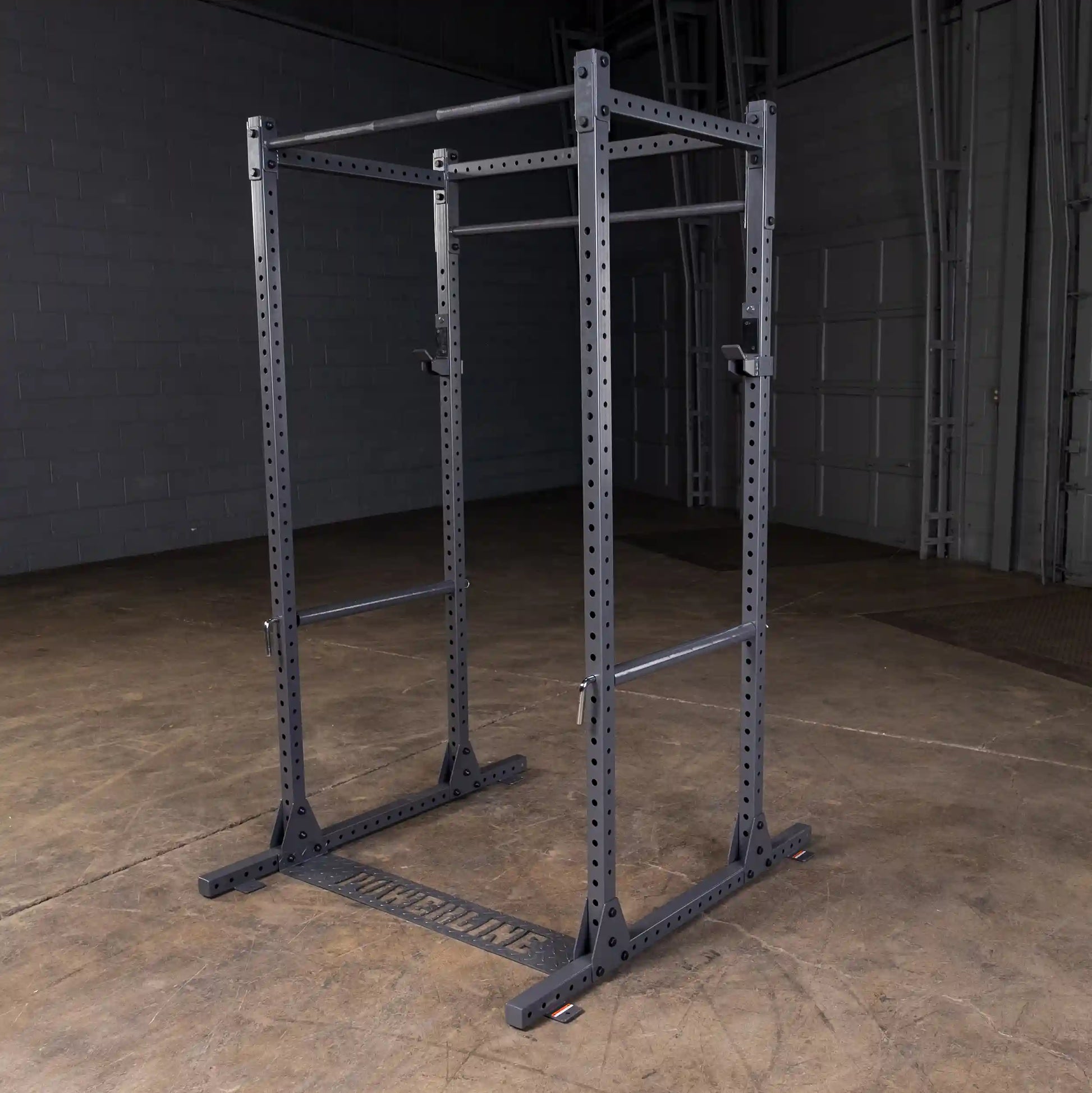 A heavy-duty power rack with a black finish, featuring adjustable bars and a sturdy base, set on a concrete floor in a gym environment.