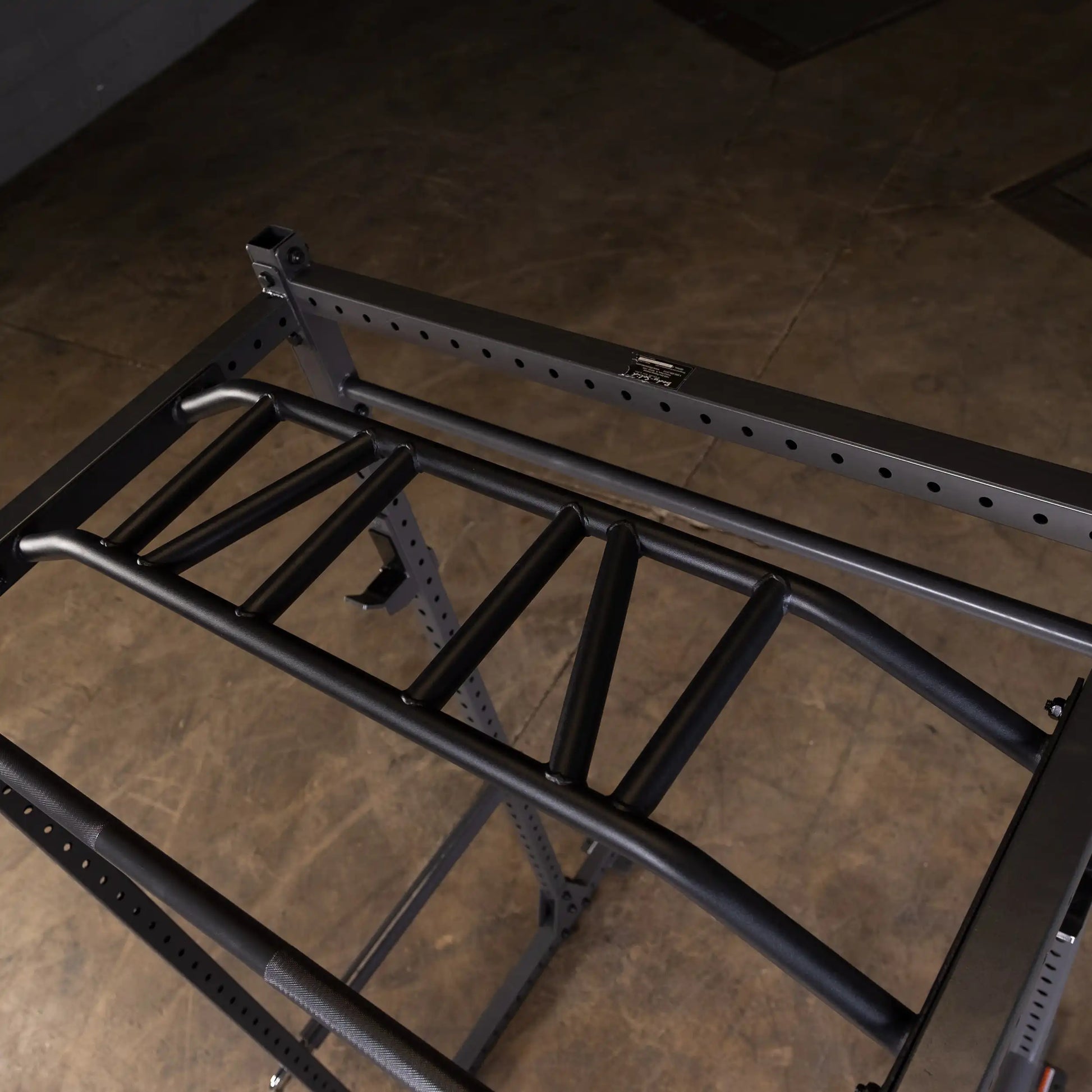 Close-up view of a black multi-grip pull-up bar attached to a sturdy metal frame, set against a concrete floor background.