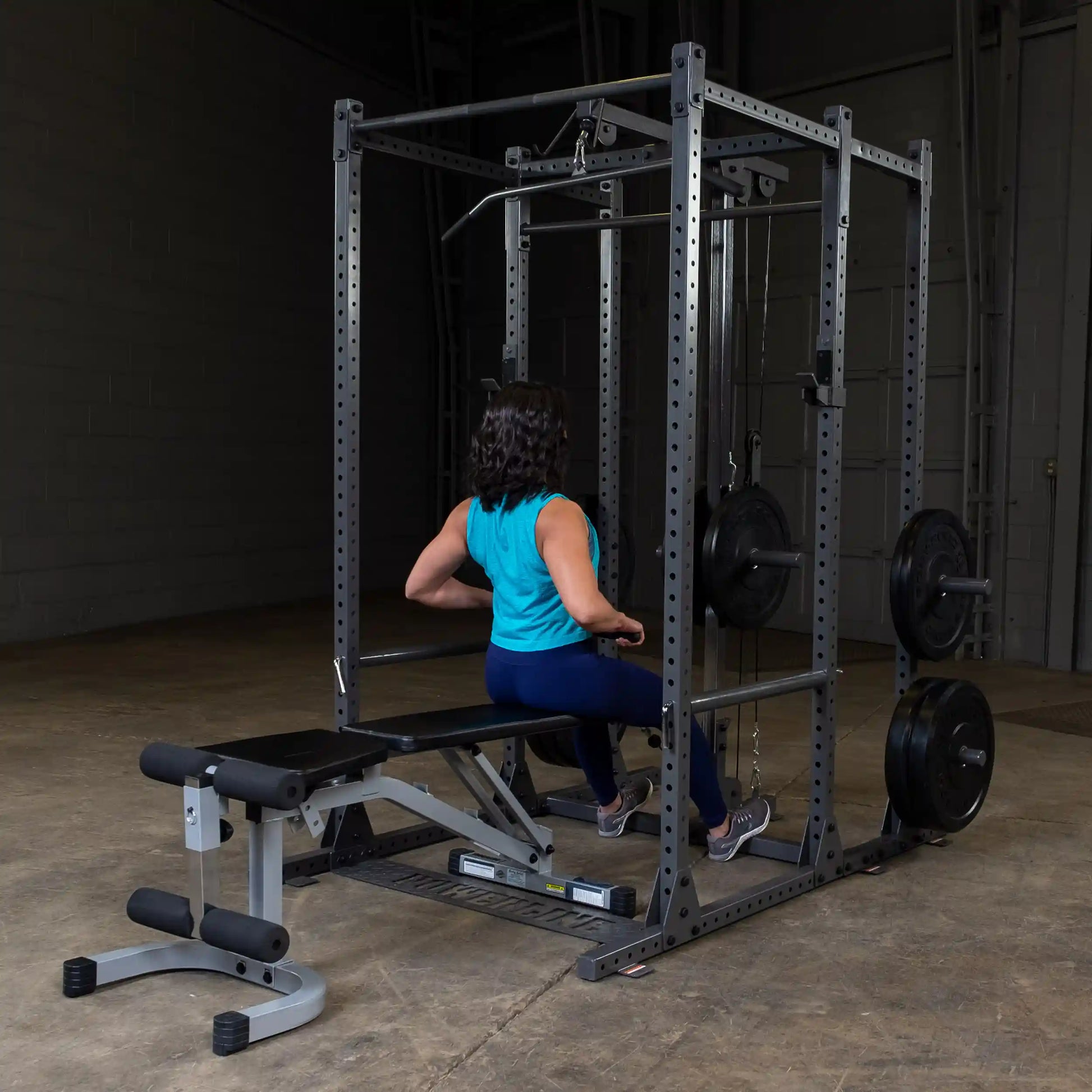 A person with curly hair is seated on a weight bench, using a cable machine for strength training in a gym setting.