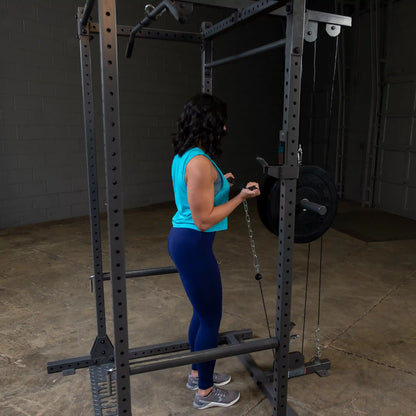 A person in a blue tank top and leggings performs an exercise using a cable machine in a gym setting. The focus is on their form as they pull a chain attached to a weight plate.
