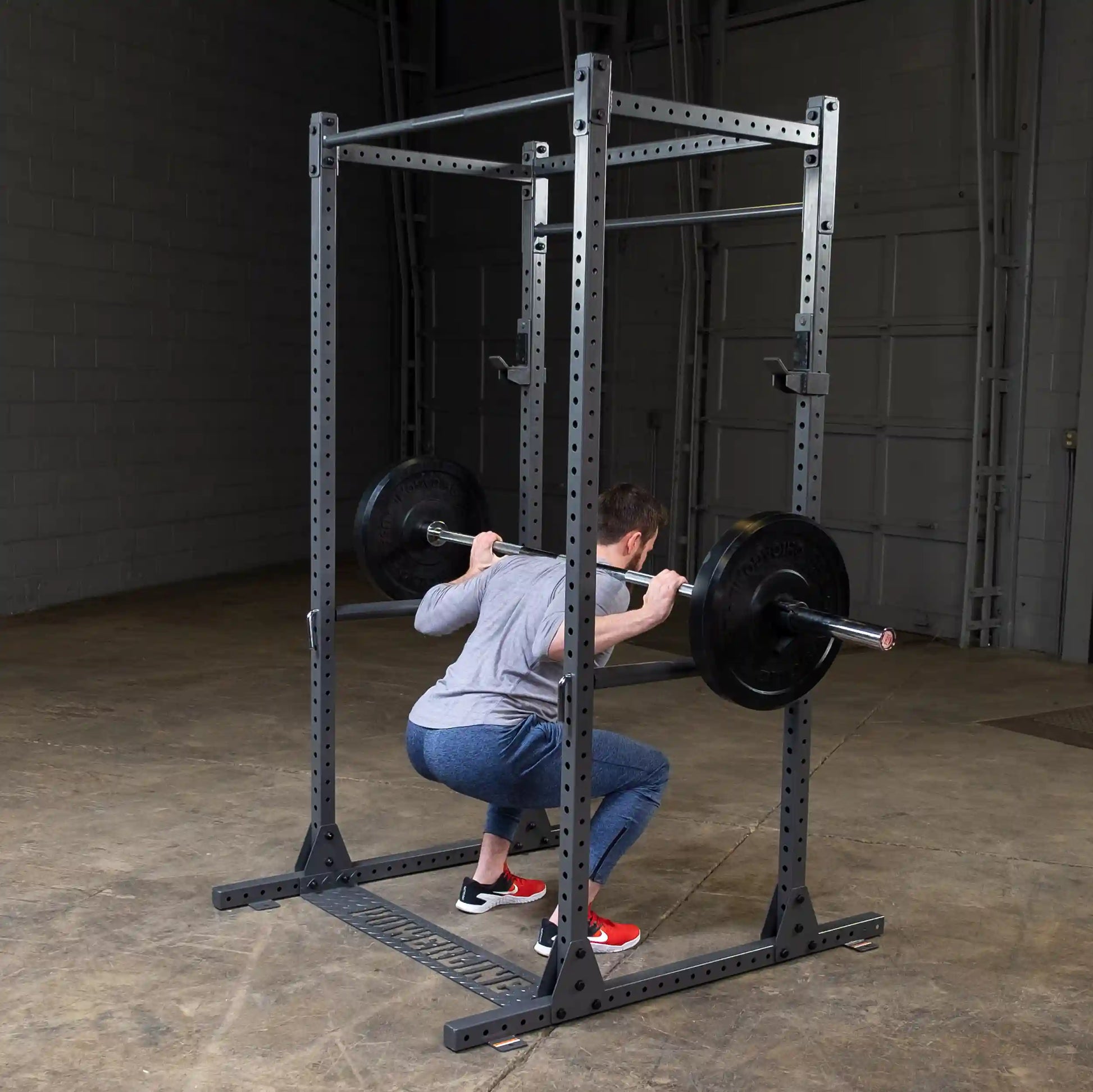 A person performing a squat exercise with a barbell on a squat rack in a gym setting.