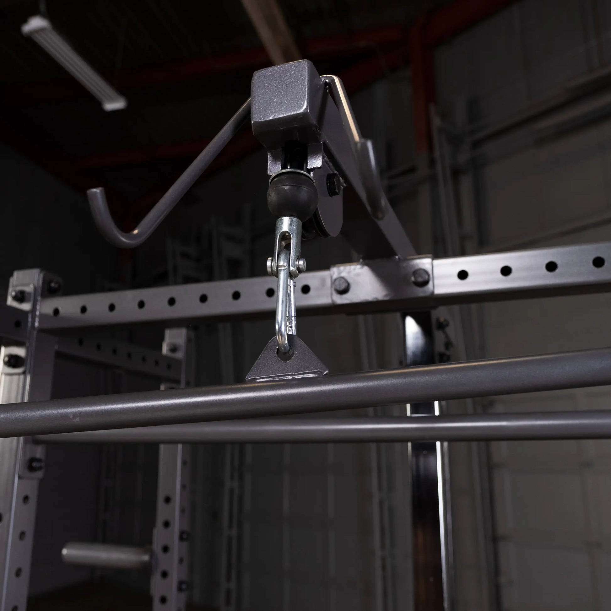 Close-up view of a gym equipment pulley system, featuring a hook and a metal bar, with a blurred background of a fitness space.