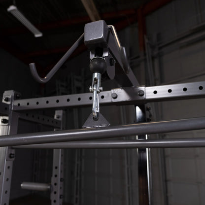 Close-up view of a gym equipment pulley system, featuring a hook and a metal bar, with a blurred background of a fitness space.