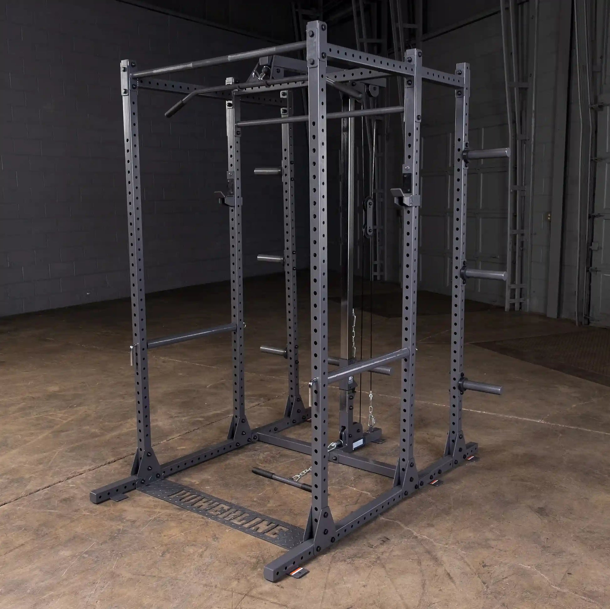 A heavy-duty gym power rack with multiple pull-up bars and adjustable weight lifting stations, set on a concrete floor in a spacious indoor gym environment.