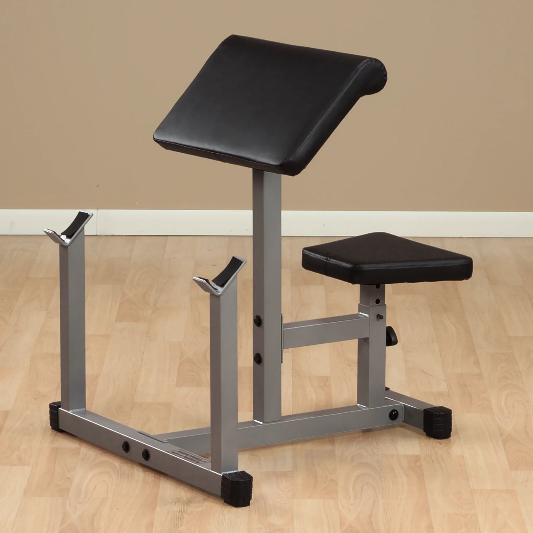 Black padded weight bench with adjustable backrest and supports for weight bars, set on a wooden floor against a neutral wall.