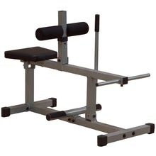 A gray and black exercise bench designed for strength training, featuring a padded seat, adjustable leg rollers, and a sturdy frame.