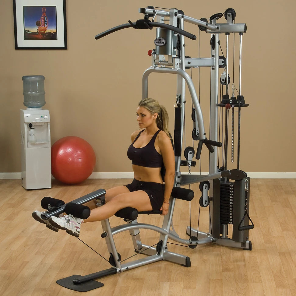 A woman exercising on a gym machine, focusing on her leg workout, in a fitness studio with a water cooler and exercise ball in the background.