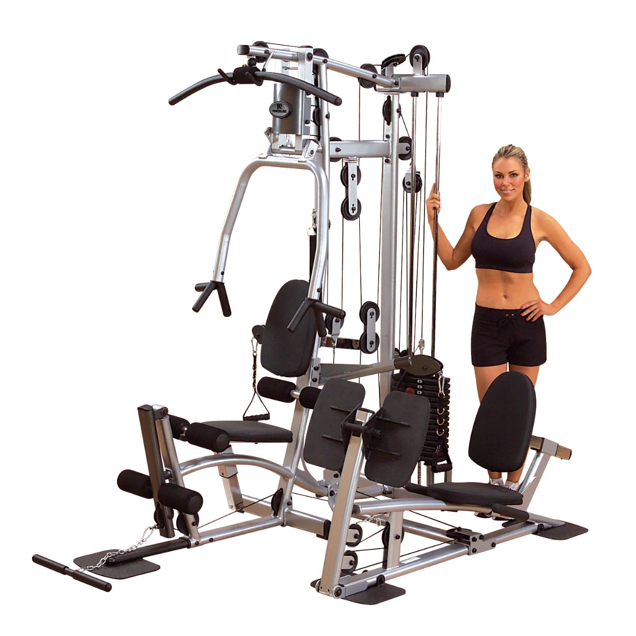 A woman in athletic wear stands next to a multi-station home gym equipment, featuring various workout stations and a weight stack.