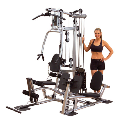A woman in athletic wear stands next to a multi-station home gym equipment, featuring various workout stations and a weight stack.