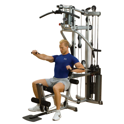 A man performing a seated row exercise on a multi-gym machine, wearing a blue athletic shirt and gray shorts, focusing on strength training.