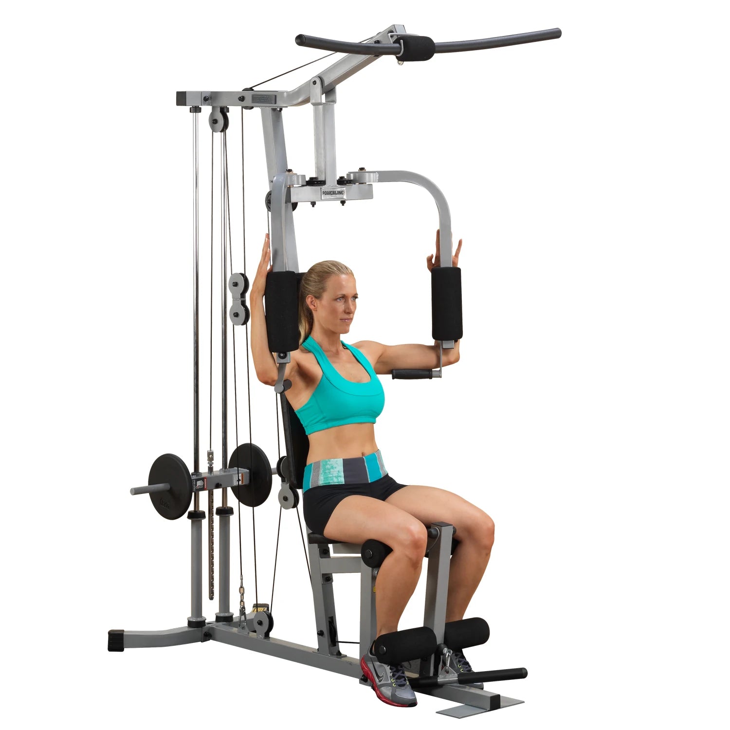 A woman performing an exercise on a multi-gym machine, wearing a turquoise sports bra and black shorts, focusing on strength training.