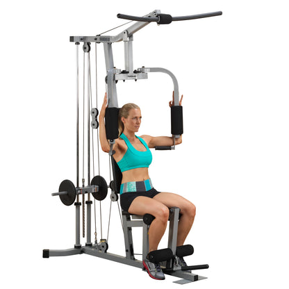 A woman performing an exercise on a multi-gym machine, wearing a turquoise sports bra and black shorts, focusing on strength training.