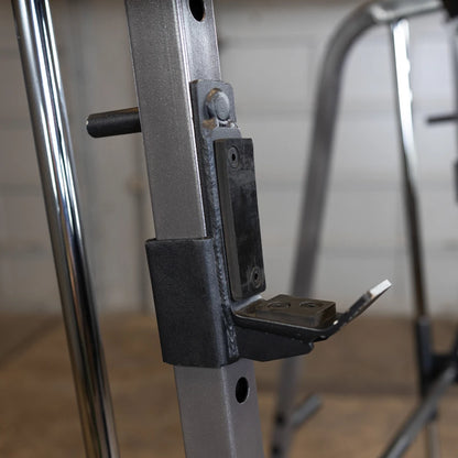 Close-up of a weightlifting rack showing a metal bracket and attachment point, designed for securing weights or gym equipment, with a blurred background of a garage setting.