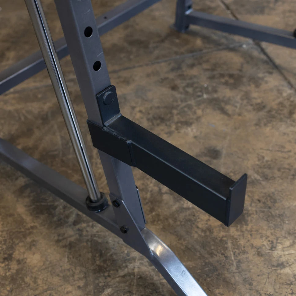 Close-up of a gym equipment frame showing a black handle attached to a gray metal structure, with a textured concrete floor in the background.