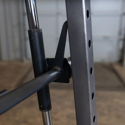 Close-up view of a weightlifting rack showing the adjustment mechanism and metal support structure, with a blurred background of a gym environment.