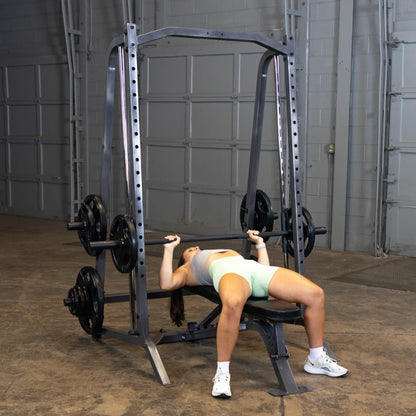A person performing a bench press exercise in a gym, lying on a bench with a barbell above them, weights on either side, in a spacious workout area.