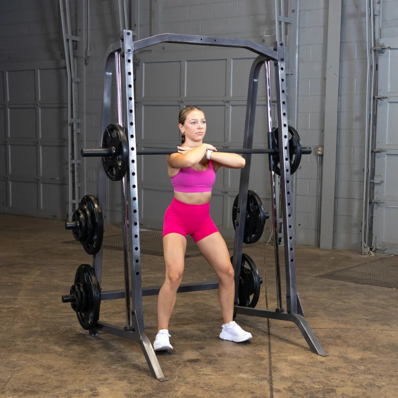A woman in a pink sports outfit performs a squat with a barbell in a gym setting, showcasing strength training and fitness.