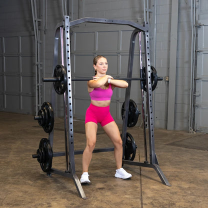 A woman in a pink sports outfit performs a squat with a barbell in a gym setting, showcasing strength training and fitness.