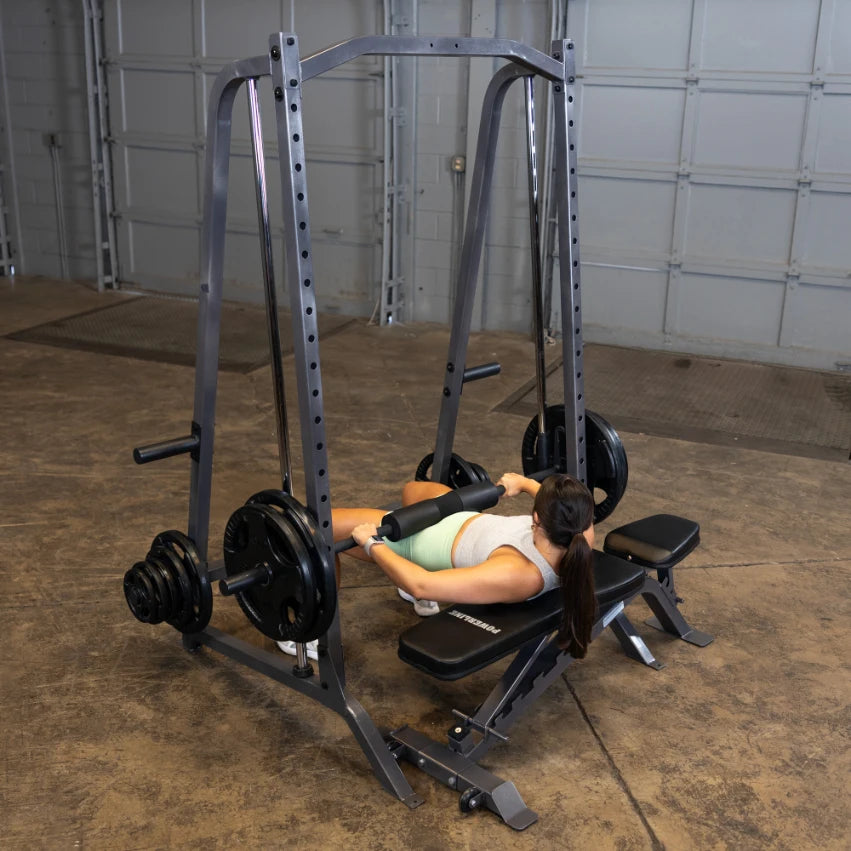 A woman performing a leg exercise on a weightlifting machine in a gym, with weights attached to the sides and a neutral colored floor.