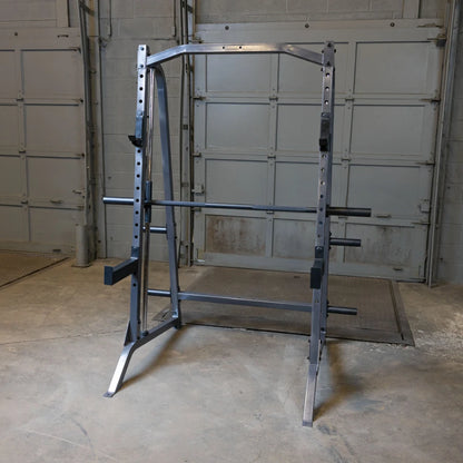 A sturdy metal squat rack positioned in a spacious gym area with concrete flooring and a garage-style background.