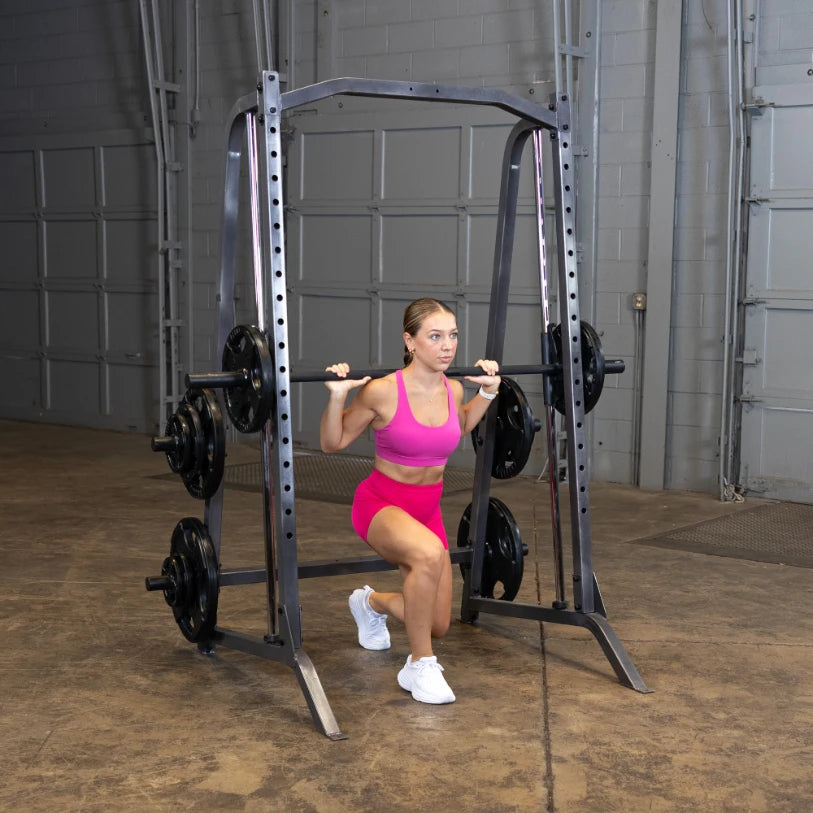 A woman in a pink workout outfit performing a squat with a barbell on a squat rack in a gym setting.