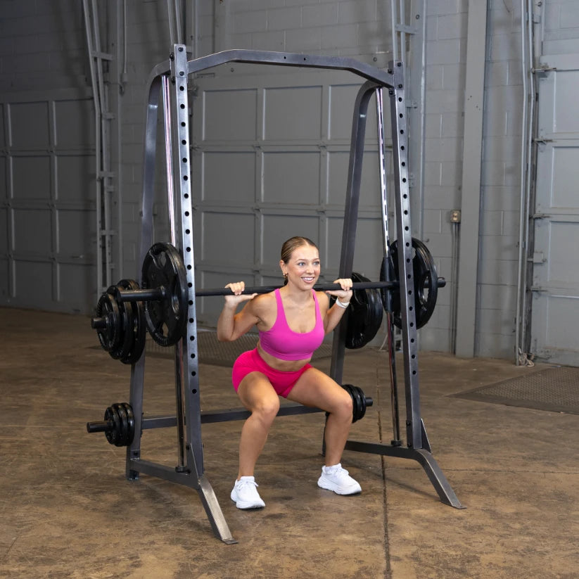 A woman in a pink workout outfit performing a squat with a barbell on her shoulders in a gym setting, showcasing strength training.