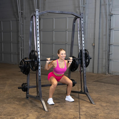 A woman in a pink workout outfit performing a squat with a barbell on her shoulders in a gym setting, showcasing strength training.