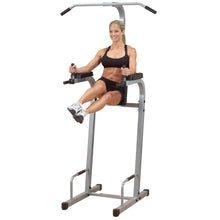 A fit woman in a black sports bra and shorts performing an exercise on a vertical knee raise machine, demonstrating strength and fitness.