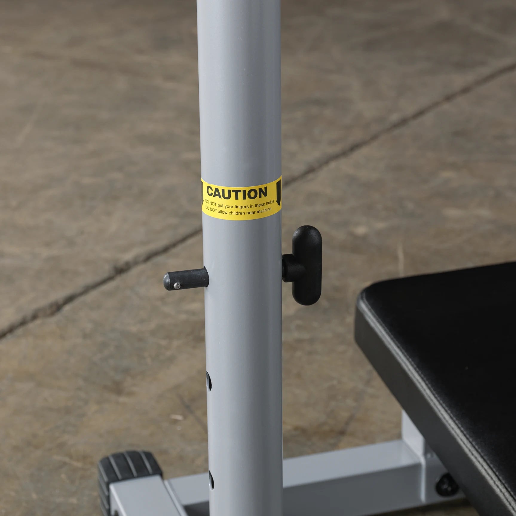 Close-up of a gym equipment post with a caution label warning against putting fingers in moving parts and advising to keep children away from the machine.
