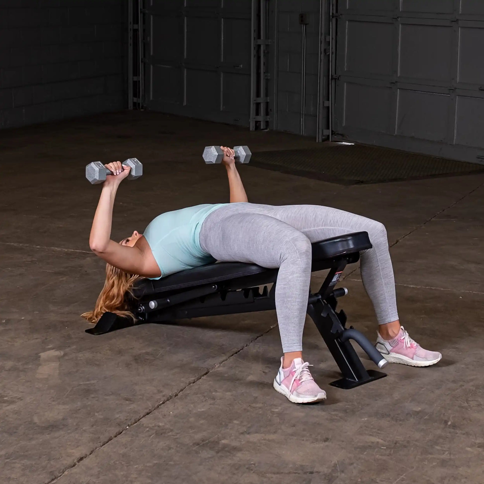A woman performs a chest press exercise using dumbbells on the Body-Solid Pro ClubLine Adjustable Bench SFID325 in a gym setting.