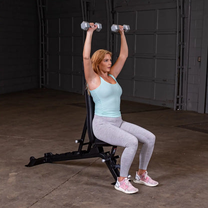 A woman performing an overhead dumbbell press while seated on the Body-Solid Pro ClubLine Adjustable Bench SFID325 in a gym setting.