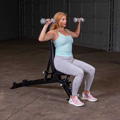 A woman seated on a Body-Solid Pro ClubLine Adjustable Bench SFID325, lifting dumbbells overhead in a gym setting. She is wearing a light blue tank top and gray leggings.
