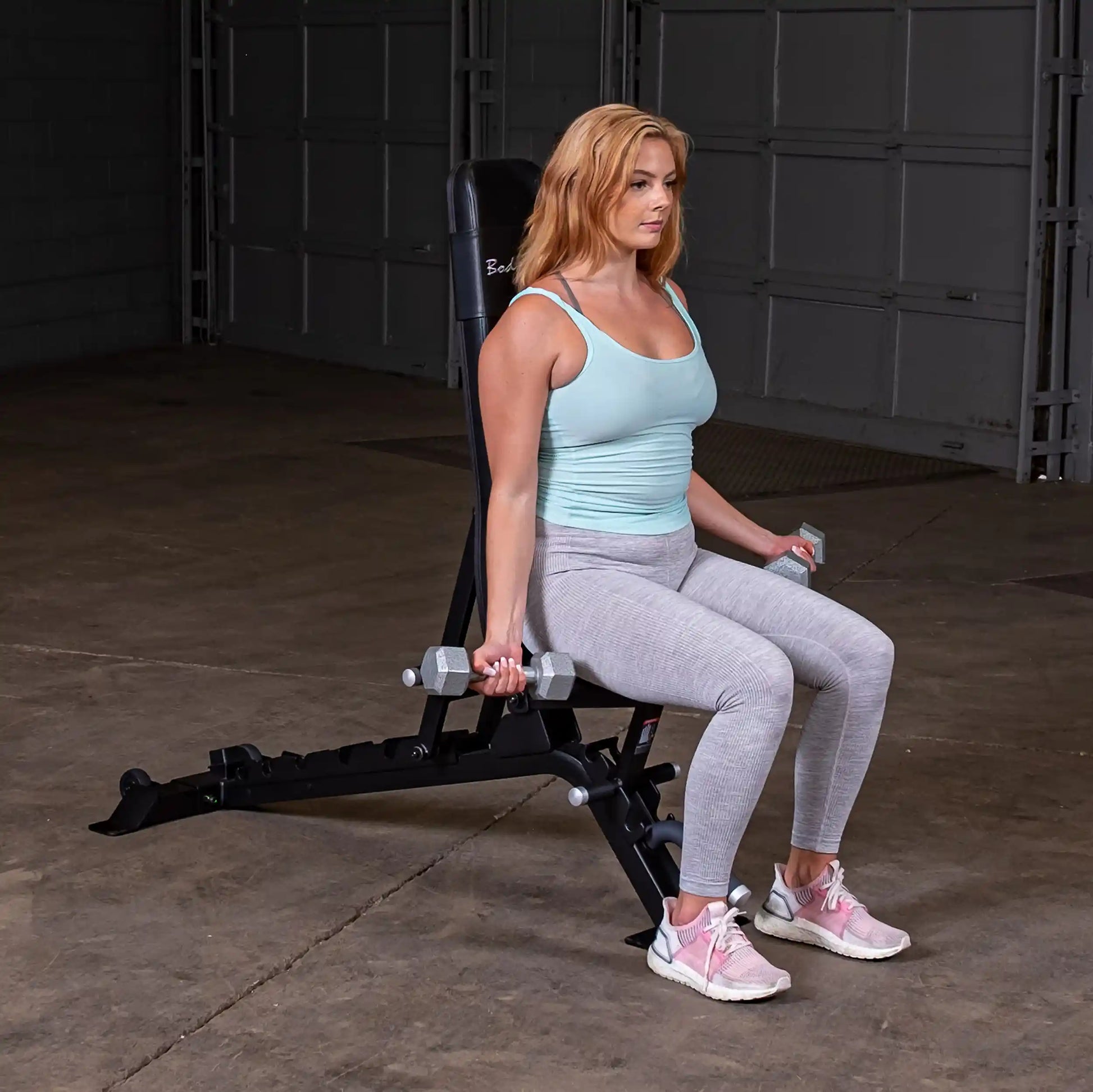 A woman performing a seated exercise with dumbbells on the Body-Solid Pro ClubLine Adjustable Bench SFID325 in a gym setting.
