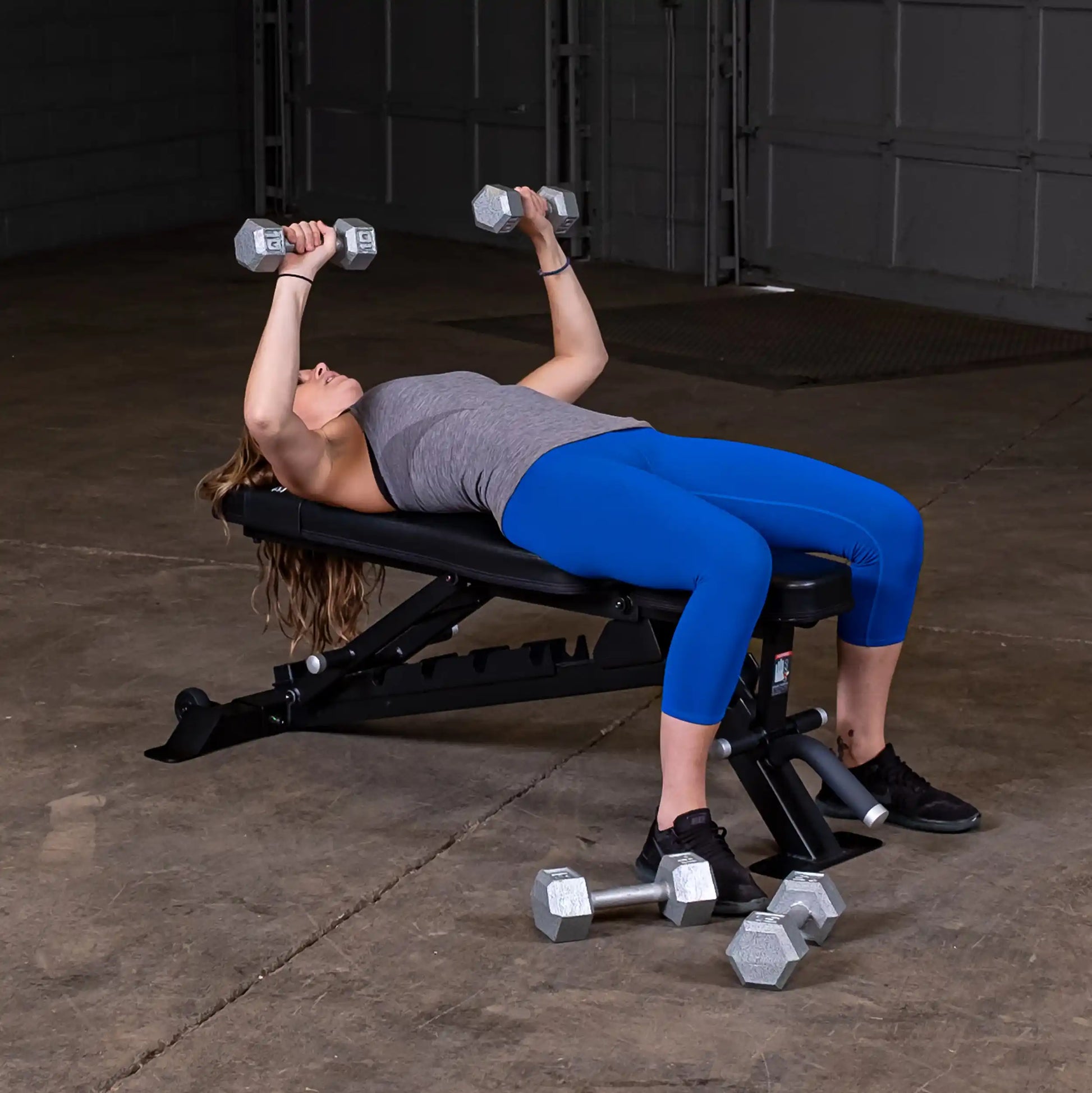 A person performing a dumbbell bench press on the Body-Solid Pro ClubLine Adjustable Bench SFID325 in a gym setting, with weights placed on the floor nearby.