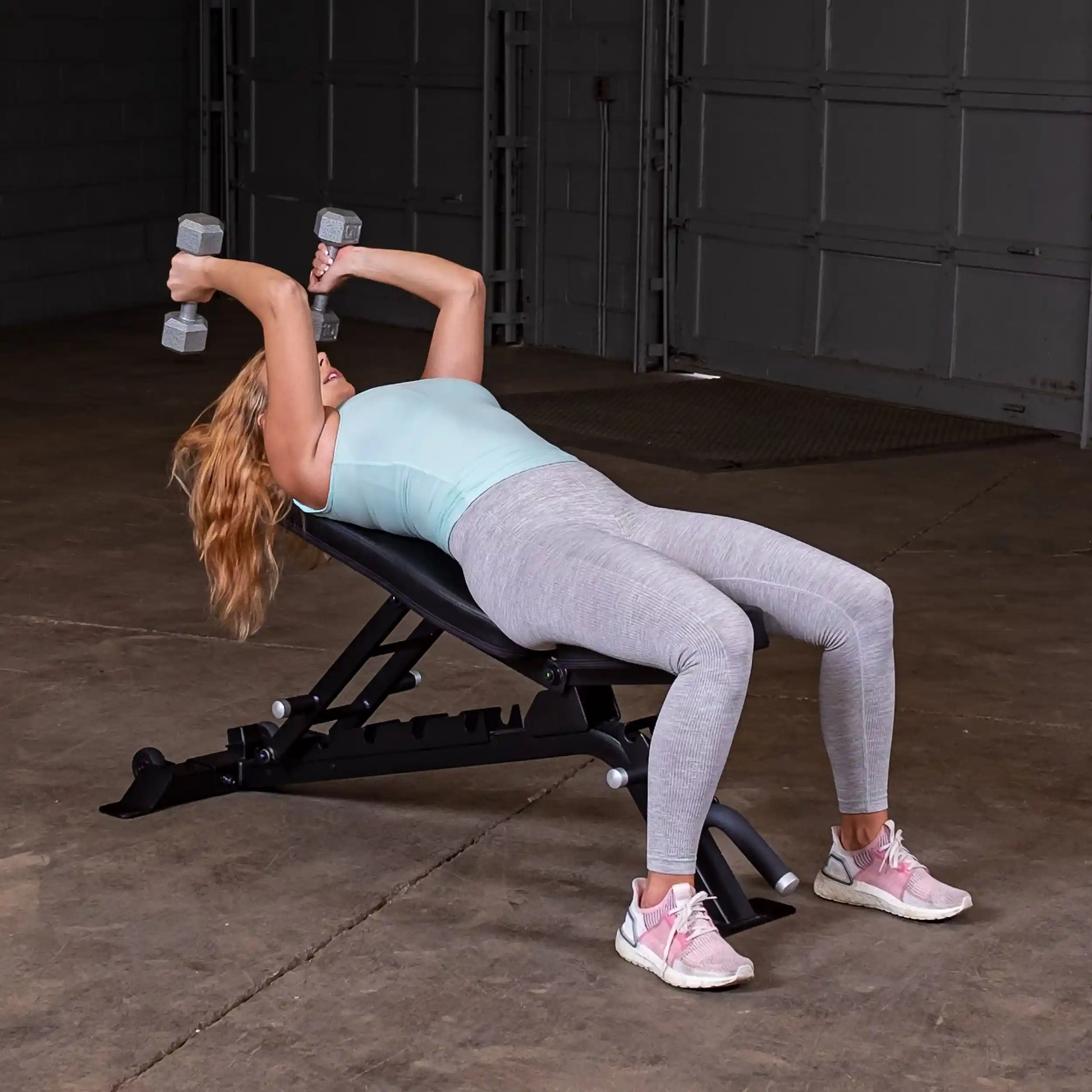 A woman performing a dumbbell exercise on the Body-Solid Pro ClubLine Adjustable Bench SFID325 in a gym setting.