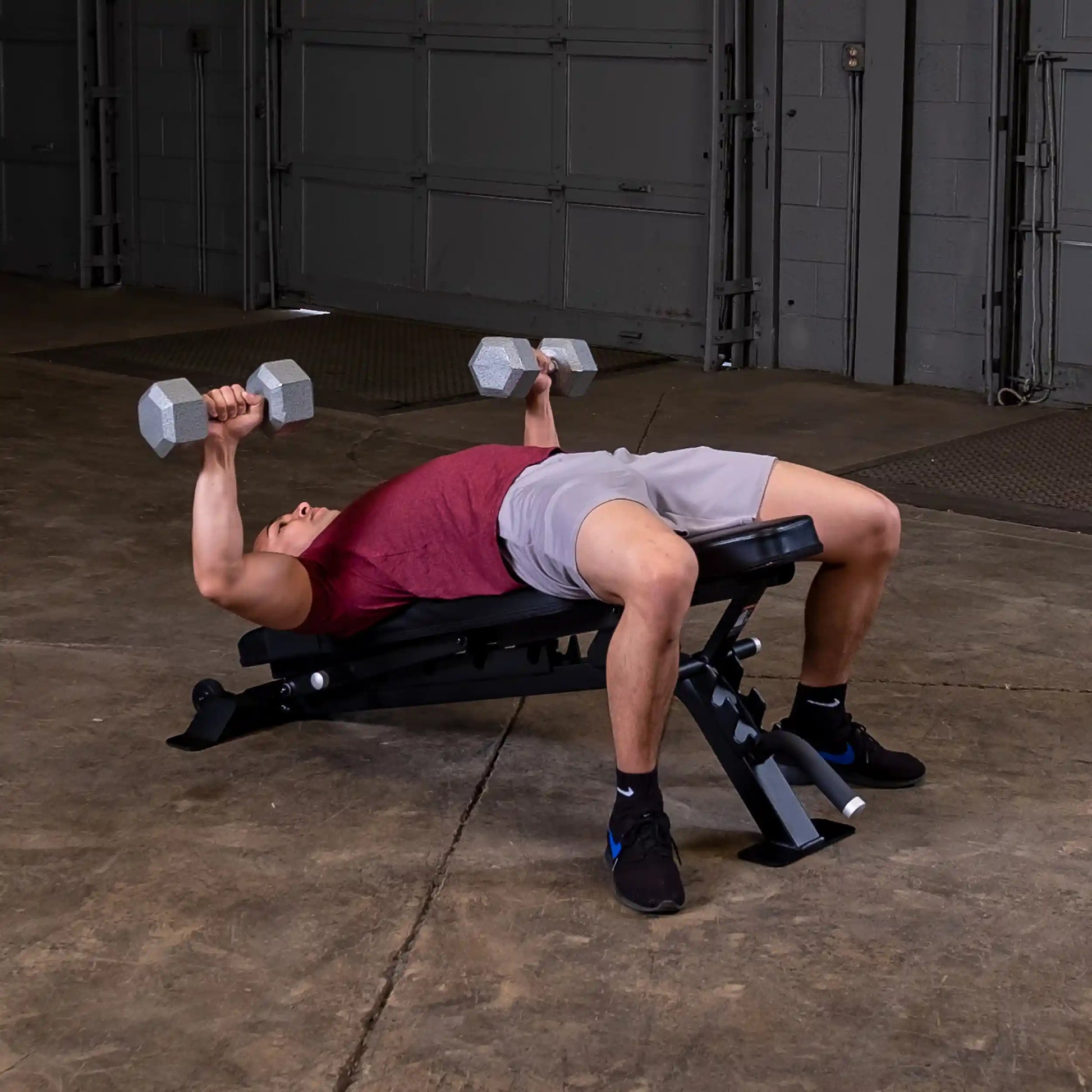 A person performing a dumbbell press on a Body-Solid Pro ClubLine Adjustable Bench SFID325 in a gym setting, with a focus on strength training and fitness.
