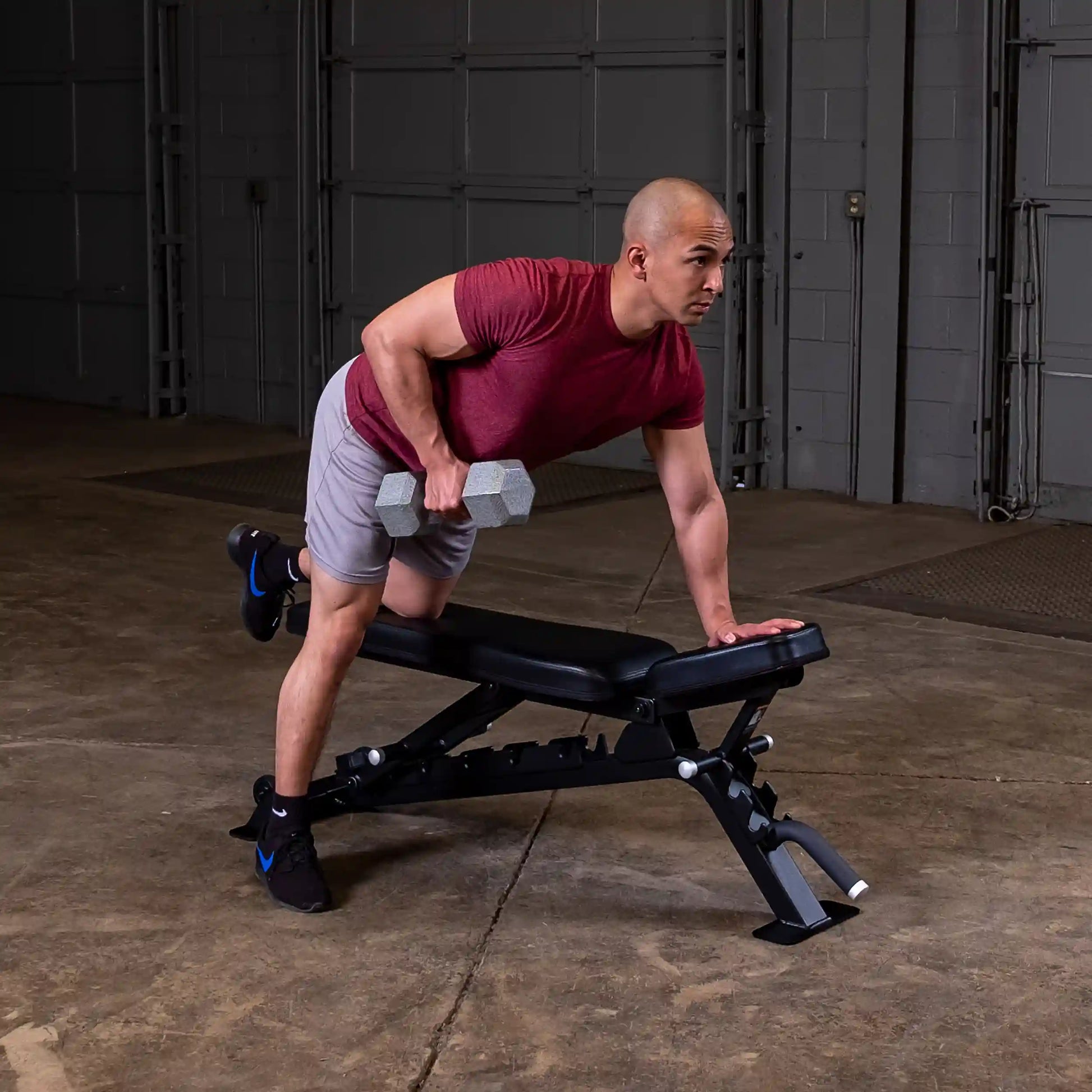 A person performing a dumbbell row exercise on a Body-Solid Pro ClubLine Adjustable Bench SFID325 in a gym setting.